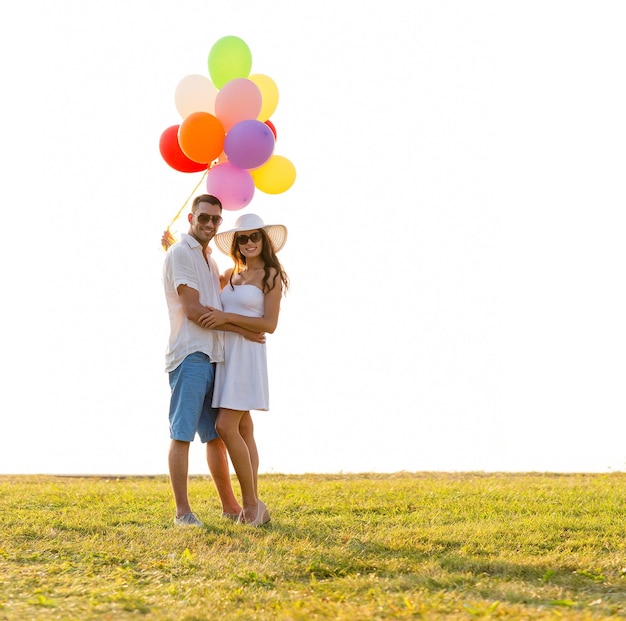 amor, boda, verano, citas y concepto de personas - pareja sonriente con gafas de sol con globos abrazándose al aire libre