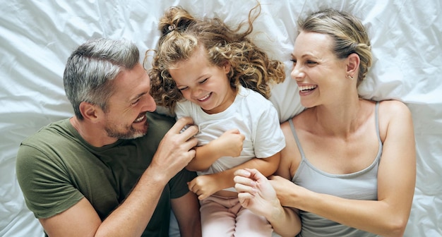 El amor en la cama y los lazos familiares se relajan y se divierten riendo y jugando juntos en un dormitorio desde arriba Sonríe jugando y el niño feliz disfruta despertándose por la mañana con padres jóvenes juguetones