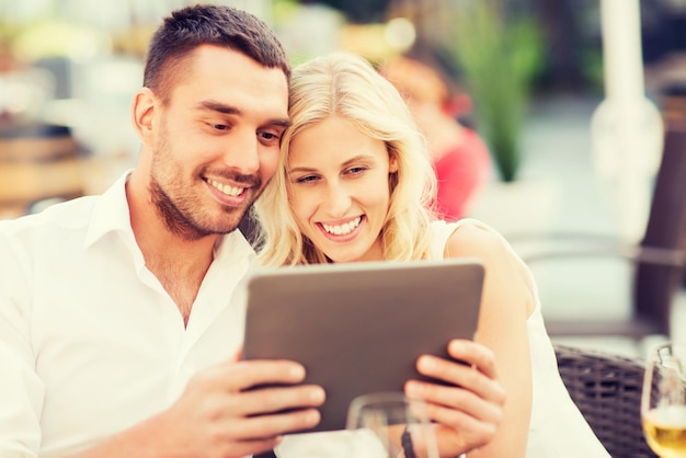 amor, citas, gente, tecnología y concepto de vacaciones - pareja feliz con tablet pc en el salón del restaurante o en la terraza