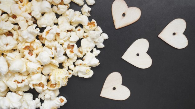 Amor concepto de palomitas de maíz. Foto horizontal. Comida dulce. Palomitas de maíz saladas clásicas con corazones de madera sobre una superficie negra