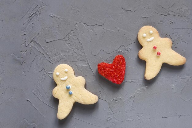 Amor corazón rojo entre figuras de galletas de un hombre y una mujer sobre un fondo gris