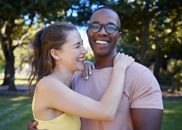 Amor de verão e risadas com um casal interracial se abraçando ao ar livre em um parque ou jardim Diversidade da natureza e romance com um homem e uma mulher se unindo durante um encontro no campo