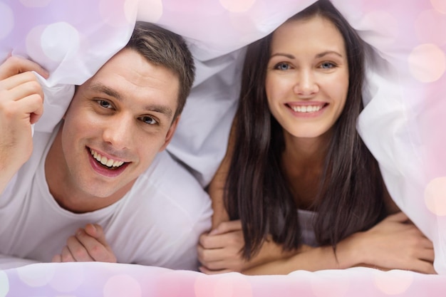 amor, dia dos namorados e conceito de pessoas - casal feliz na cama sobre fundo de luzes de férias