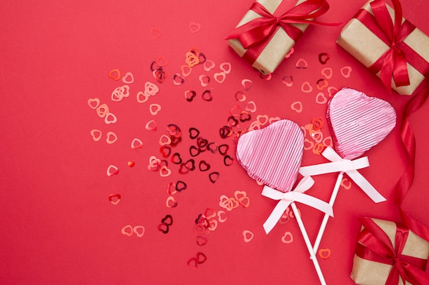 Amor, dia dos namorados simulado acima, com pirulito em forma de um coração, presente boxex e glitter isolado sobre fundo vermelho, copie o espaço.