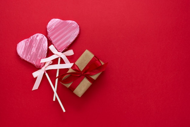 Amor, día de San Valentín simulacro, con piruleta en forma de corazón y caja de regalo, aislado sobre fondo rojo, copia espacio.