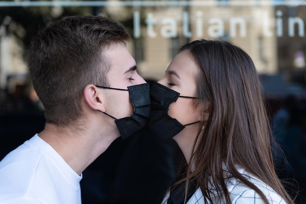 Amor durante a quarentena jovem e mulher com máscaras médicas pretas se beijam