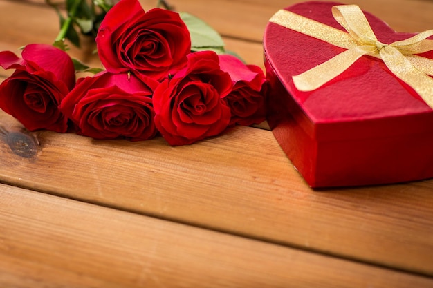 amor, encontro, romance, dia dos namorados e conceito de feriados - close-up da caixa de presente em forma de coração e rosas vermelhas na mesa de madeira