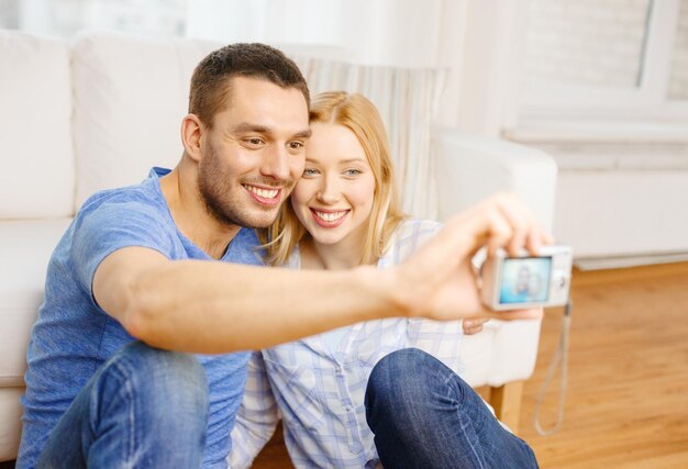 amor, familia, tecnología y concepto de felicidad - pareja sonriente tomando una foto de autorretrato con cámara digital en casa