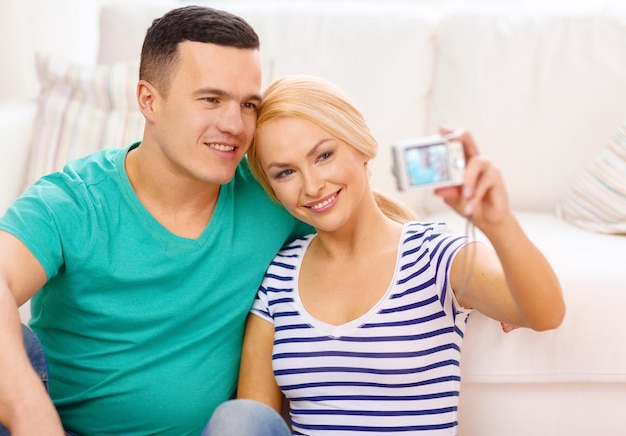 amor, familia, tecnología y concepto de felicidad - pareja sonriente tomando una foto de autorretrato con cámara digital en casa