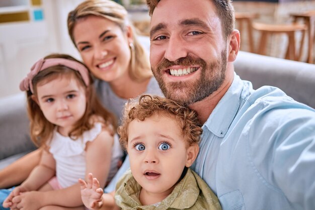 Amor familiar y selfie en la sala de estar, unión y cuidado del hogar mientras se toma una foto para un recuerdo feliz Apoyo de sonrisas y autorretrato de padres con hijos en el sofá para redes sociales o publicaciones en línea