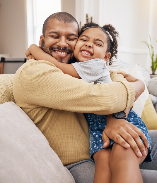 Amor feliz e menina abraçando seu pai enquanto se relaxam em um sofá na sala de estar juntos Cuidados de sorriso e ligação infantil abraçando e sentando-se com seu jovem pai no salão de sua casa