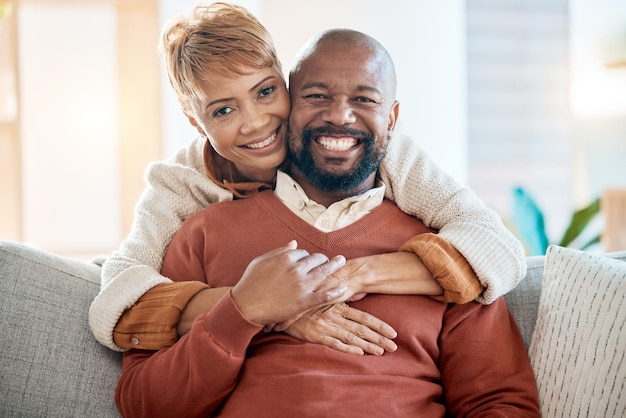 Amor feliz e retrato de casal negro no sofá para relaxar a aposentadoria ou apoiar juntos Abraço sorridente ou casamento com o velho e a mulher na sala de estar em casa para relacionamento ou estilo de vida