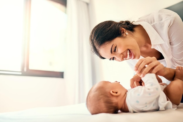 Amor feliz e uma mãe com seu bebê no quarto de sua casa juntos para um vínculo lúdico Filhos da família e uma jovem mamãe passando um tempo com seu bebê recém-nascido na cama para diversão ou alegria