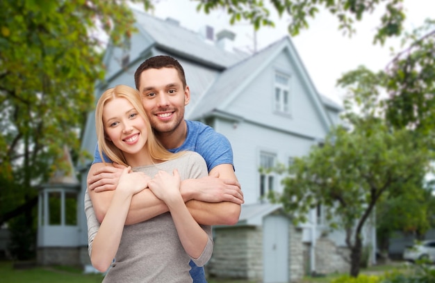 amor, gente, bienes raíces, hogar y concepto familiar - pareja sonriente abrazándose sobre el fondo de la casa