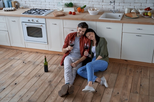 Amor joven pareja romántica feliz hombre y mujer caucásicos sentados en el suelo en la cocina moderna