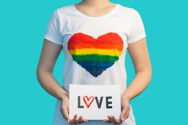 Amor LGBT Relação gay Mês do orgulho Diversidade de gênero Mulher de camiseta com bandeira de coração colorido arco-íris mão segurando placa isolada em fundo azul