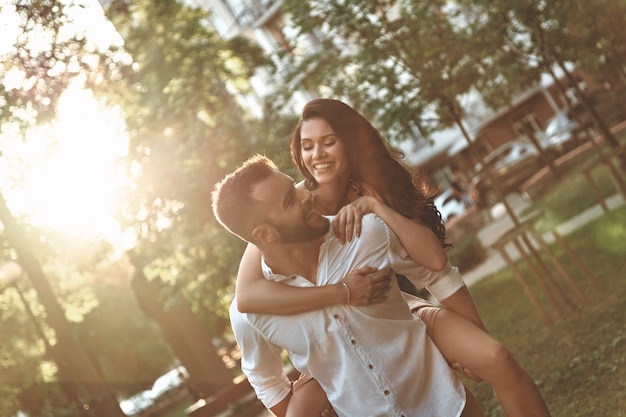 El amor lo hace todo posible. Apuesto joven dando a su novia un paseo a cuestas mientras pasan tiempo juntos