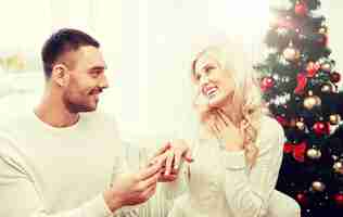 Foto amor, natal, casal, presente e pessoas conceito - homem feliz dando anel de noivado de diamante para a mulher em casa