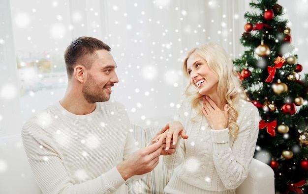 amor, navidad, pareja, presente y concepto de la gente - hombre feliz dando anillo de diamantes de compromiso a la mujer en casa