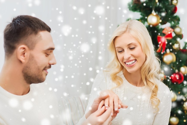 amor, navidad, pareja, propuesta y concepto de la gente - hombre feliz dando anillo de compromiso de diamantes a la mujer en casa
