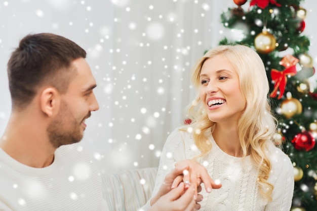 amor, navidad, pareja, propuesta y concepto de la gente - hombre feliz dando anillo de compromiso de diamantes a la mujer en casa