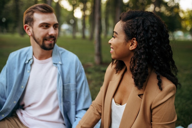 Amor pareja cogidos de la mano, caminando en el parque. Hombre y mujer sentados en la hierba. Familia relajarse en la pradera en verano, fin de semana en la naturaleza