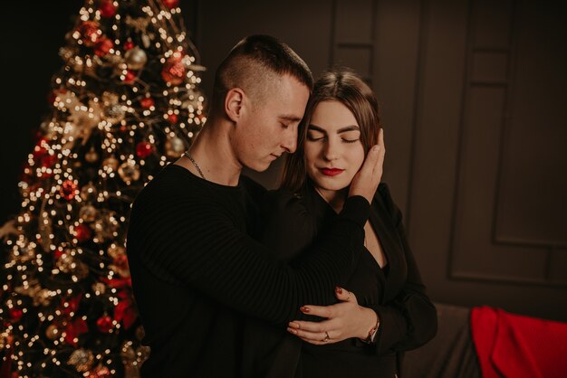 Amor pareja hombre y mujer abrazándose besándose cerca del árbol de Navidad