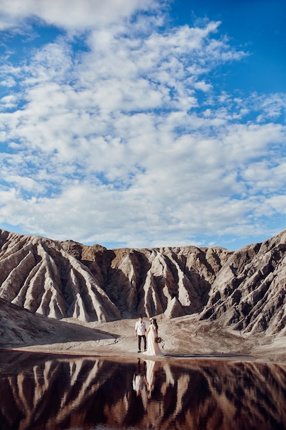 Amor de pareja en montañas fabulosas abrazándose cerca del lago rojo, paisajes fabulosos. Los amantes caminan en las montañas en verano, chica con un vestido largo y ligero de verano con un ramo de flores y una corona en la cabeza