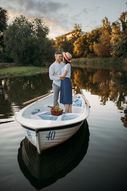 Amor pareja de pie en un barco en el lago tranquilo en el día de verano al atardecer. Encuentro romántico, paseo en bote, hombre y mujer caminando por el lago