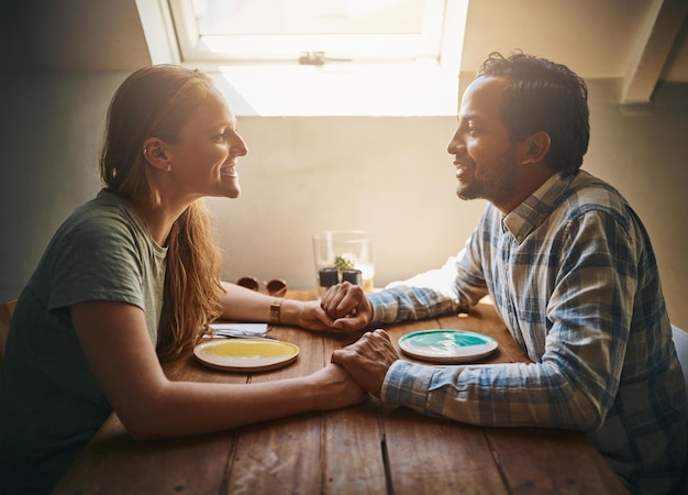 Amor pareja y tomados de la mano en el café en la mesa hablando y uniéndose juntos Día de San Valentín diversidad romántica y afecto del hombre y la mujer en la cita divirtiéndose o disfrutando del tiempo en el restaurante