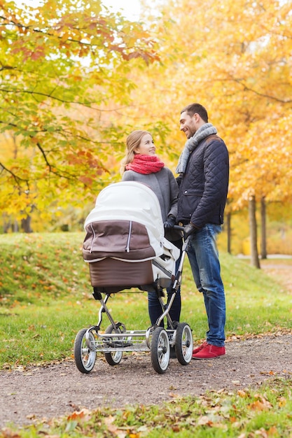 amor, paternidad, familia, temporada y concepto de personas - pareja sonriente con cochecito de bebé en el parque de otoño