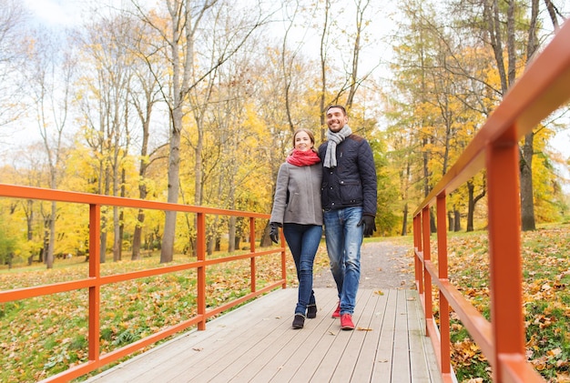 amor, relación, familia, temporada y concepto de personas - pareja sonriente abrazándose en el puente en el parque de otoño