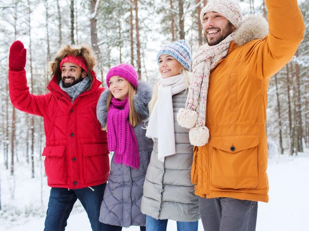 amor, relación, temporada, amistad y concepto de personas - grupo de hombres y mujeres sonrientes agitando las manos en el bosque de invierno