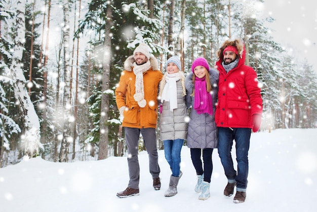 amor, relación, temporada, amistad y concepto de personas - grupo de hombres y mujeres sonrientes caminando en el bosque de invierno