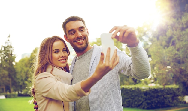 amor, relacionamento, tecnologia e conceito de pessoas - casal feliz com smartphone tomando selfie no parque de verão