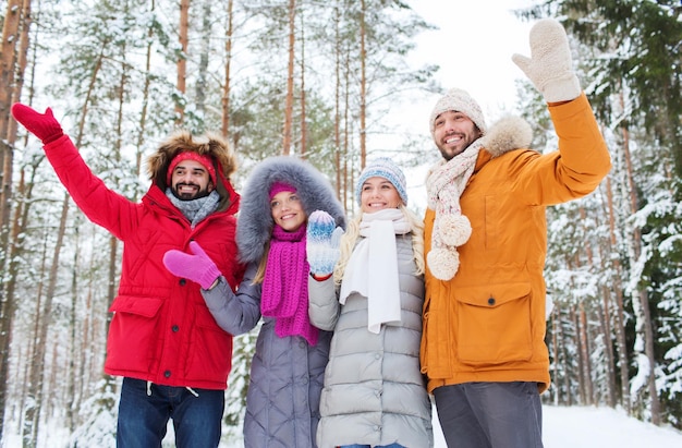 Amor, relacionamento, temporada, amizade e conceito de pessoas - grupo de homens e mulheres sorridentes acenando com as mãos na floresta de inverno