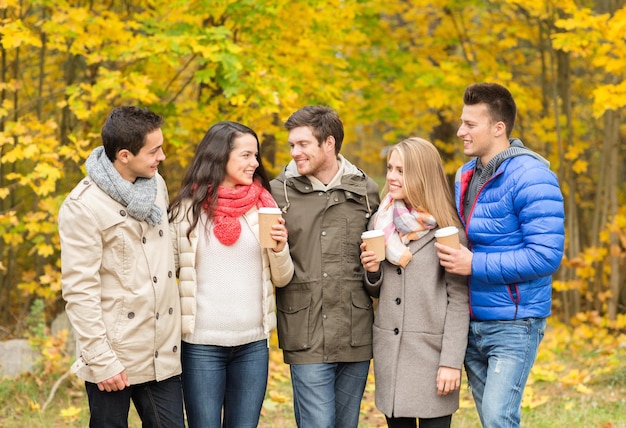 amor, relacionamento, temporada, amizade e conceito de pessoas - grupo de homens e mulheres sorridentes andando com xícaras de café de papel no parque outono