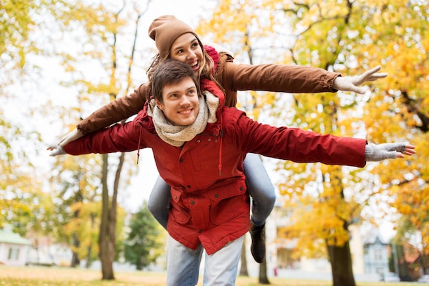 amor, relaciones, temporada y concepto de personas - feliz pareja joven divirtiéndose en el parque de otoño