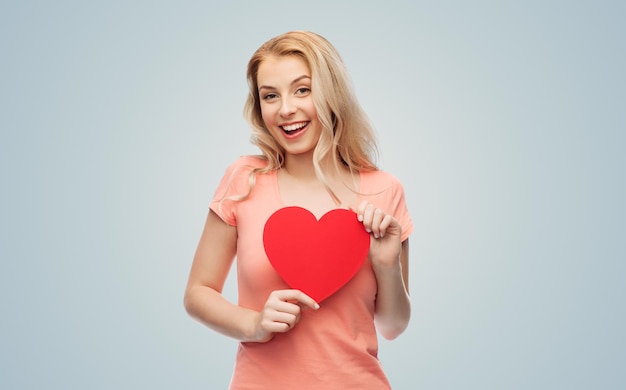 amor, romance, caridade, dia dos namorados e conceito de pessoas - sorrindo jovem ou adolescente com forma de coração vermelho em branco sobre fundo cinza