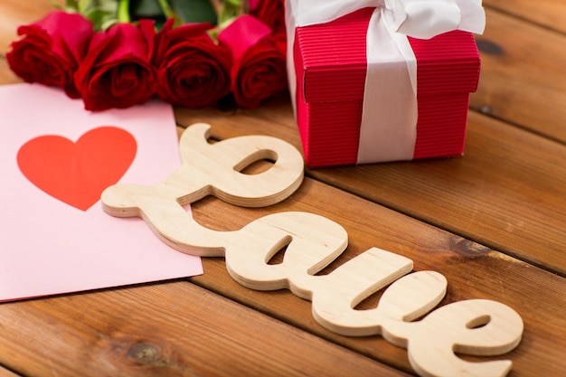 amor, romance, día de san valentín y concepto de vacaciones - cierre de caja de regalo, rosas rojas y tarjeta de saludo con corazón en madera