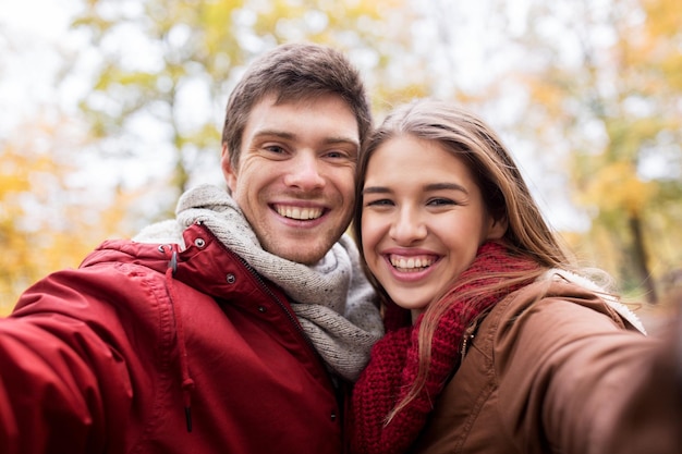 amor, tecnologia, relacionamento, família e conceito de pessoas - casal jovem sorridente feliz tomando selfie no parque outono