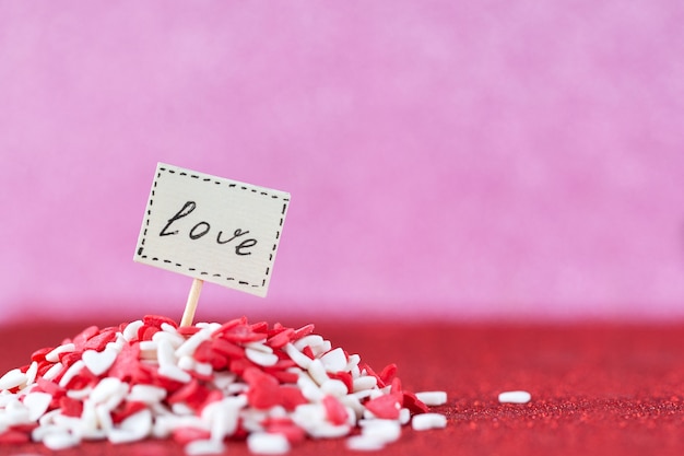 Amor texto compuesto a bordo en un montón de corazones rojos y blancos en la pared rosa para el concepto del día de San Valentín.