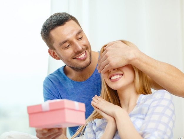 amor, vacaciones, celebración y concepto familiar - el hombre sonriente sorprende a su novia con un regalo en casa