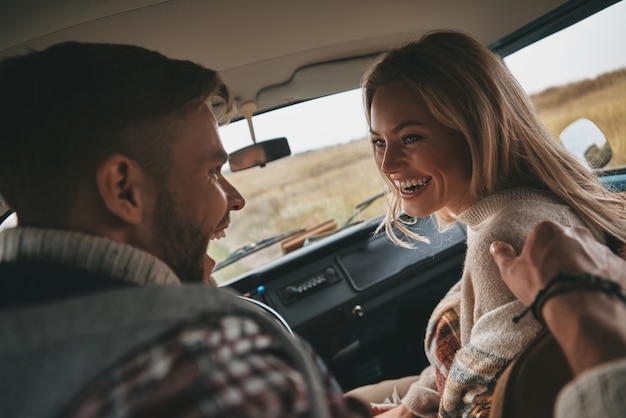 Amor verdadero. Feliz pareja joven riendo mientras está sentado en los asientos del pasajero delantero en mini van estilo retro