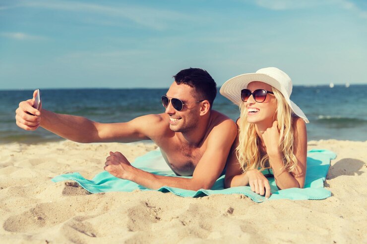Foto amor, viagens, turismo, tecnologia e conceito de pessoas - casal sorridente de férias em trajes de banho e óculos de sol e tomando selfie com smartphone na praia de verão