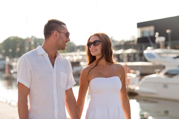 el amor, los viajes, el turismo y el concepto de la gente - pareja sonriente con gafas de sol caminando por el puerto