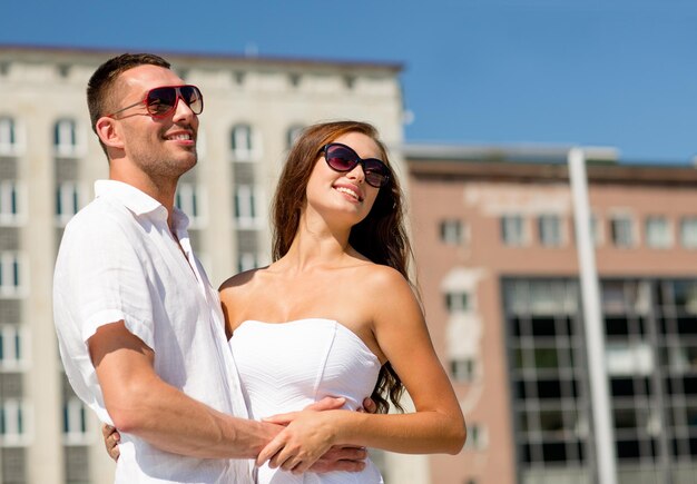 amor, viajes, turismo, gente y concepto de amistad - pareja sonriente con gafas de sol abrazándose en la ciudad