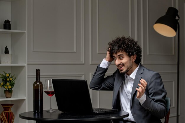 Amor virtual bonitão bonito de terno com vinho em um encontro de computador à distância segurando a cabeça sorrindo