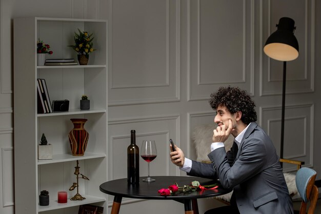 Foto amor virtual bonitão bonito de terno com vinho na data do telefone à distância pensando com a mão no queixo