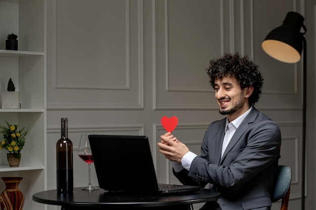 Amor virtual guapo chico lindo en traje con vino en una fecha de computadora a distancia con corazón rojo